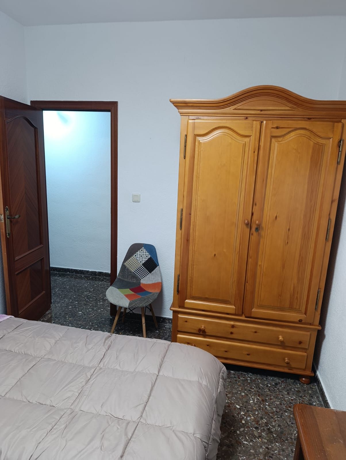 Una habitación con una cama, un armario de madera, una silla y una puerta.