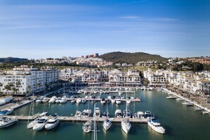 Un port de plaisance où sont amarrés de nombreux bateaux, entouré de bâtiments résidentiels et dominé par un paysage vallonné.