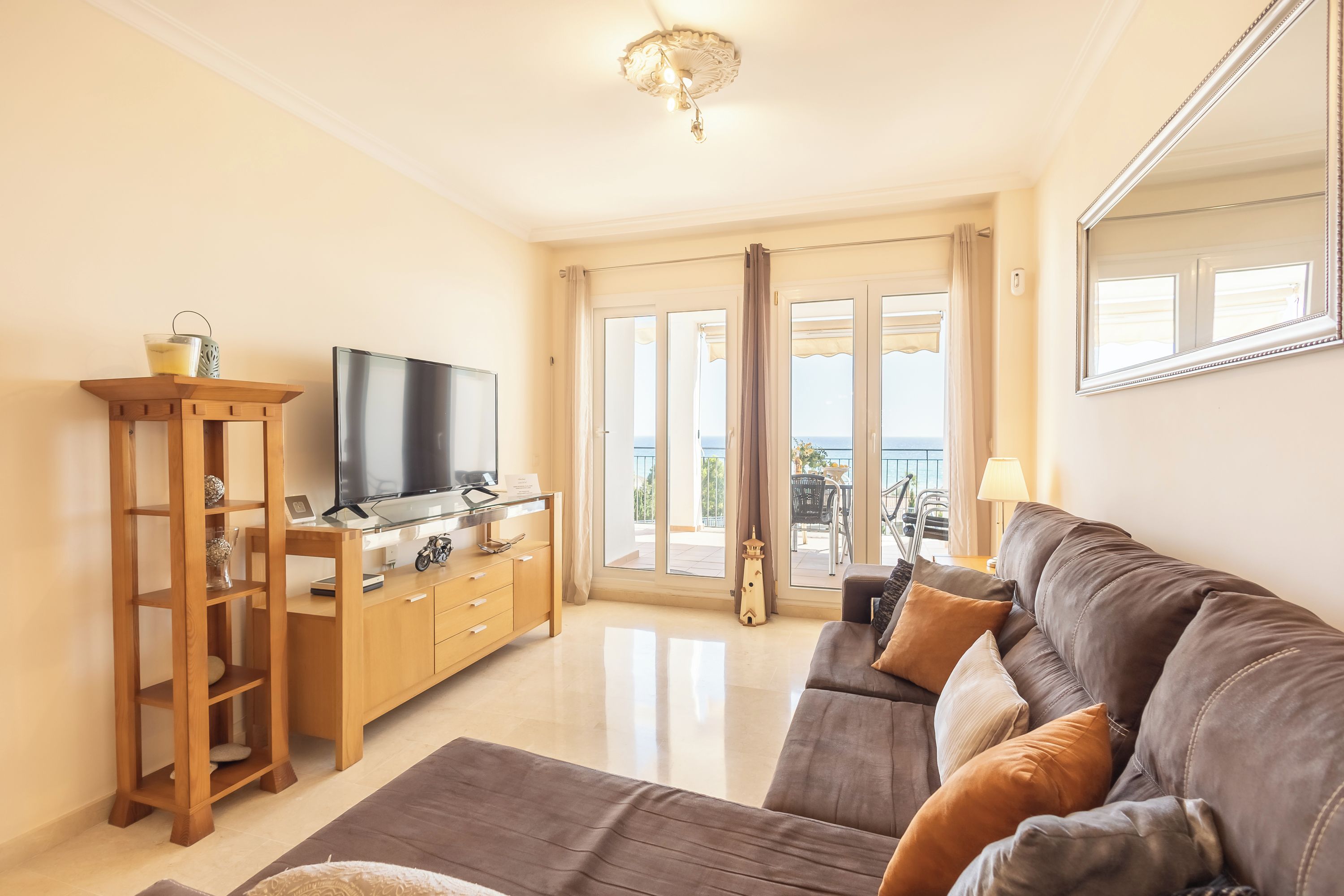 A living room with a flat-screen TV, wooden furniture, a sofa, and a view through the glass doors.