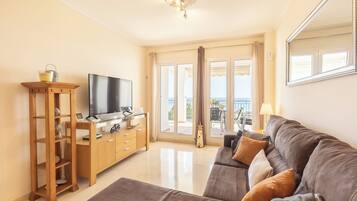 A living room with a flat-screen TV, wooden furniture, a sofa, and a view through the glass doors.