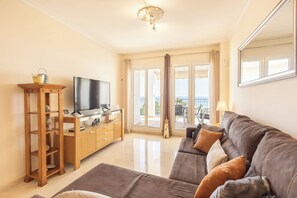 Una sala de estar con televisor de pantalla plana, muebles de madera, un sofá y vistas a través de puertas de vidrio.