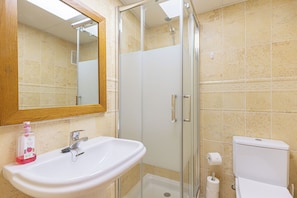 Un baño con lavamanos blanco, cabina de ducha de vidrio y retrete.