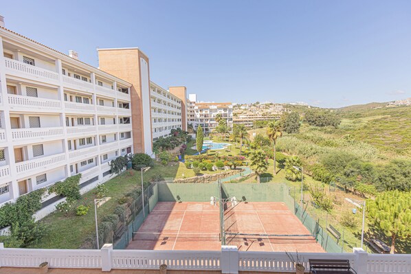 Un hotel de varios pisos con balcones, cancha de tenis y zona de piscina.