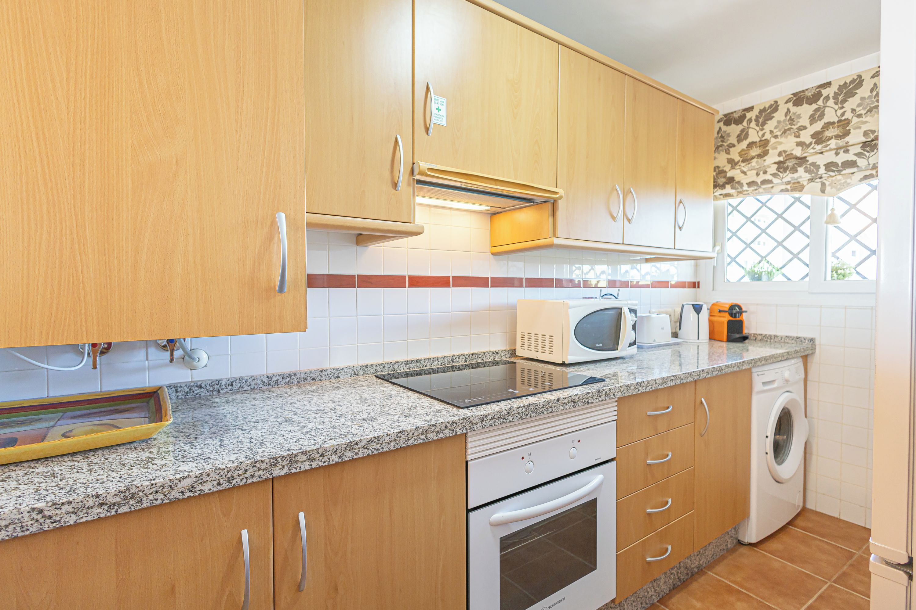 Una cocina con gabinetes de madera, microondas, tostadora y lavadora.