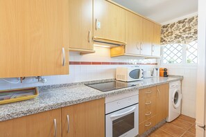 Une cuisine avec des meubles de rangement en bois, un four à micro-ondes, un grille-pain et un lave-linge.