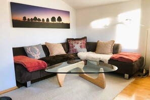Ein Wohnzimmer mit einem Glastisch, einer Couch mit gemusterten Kissen und einem Gemälde an der Wand.