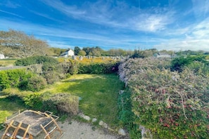 A garden with a wooden table and chairs, surrounded by various plants and a white building in the background. - Holiday home in Carnac with swimming pool (Carnac)