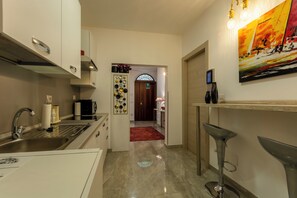 A modern kitchen with a stainless steel sink, a microwave, and a white cabinet. There is a hallway leading to a room with a red carpet and a door with a glass window.