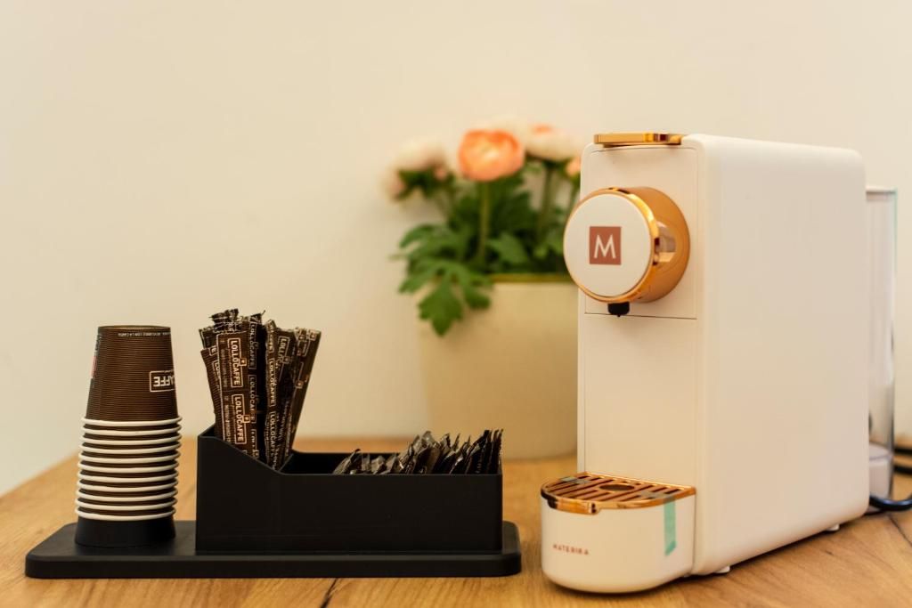 Une machine à café au design blanc et doré, une tasse à café et un récipient contenant des dosettes de café, le tout posé sur une surface en bois.