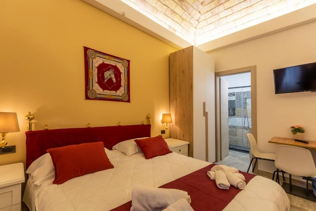 A hotel room with a bed, bedside tables, a desk, a chair, a TV, and a balcony with a city view.