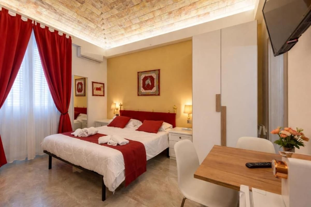 A hotel room with a bed, bedside tables, a desk, and a TV.