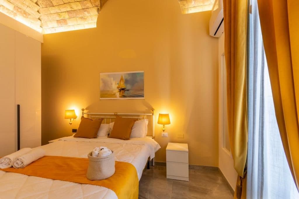 Una habitación de hotel con cama, lámparas de noche, un cuadro y una mesita de noche.
