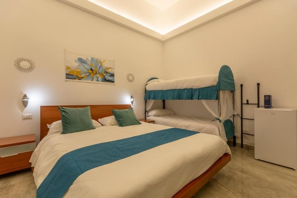 Una habitación de hotel con literas, una mesita de noche, una lámpara, una obra de arte en la pared y un refrigerador pequeño.
