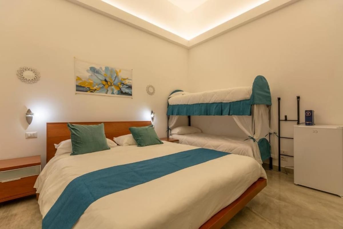 A hotel room with a bunk bed, a bedside table, a lamp, a wall art piece, and a small refrigerator.