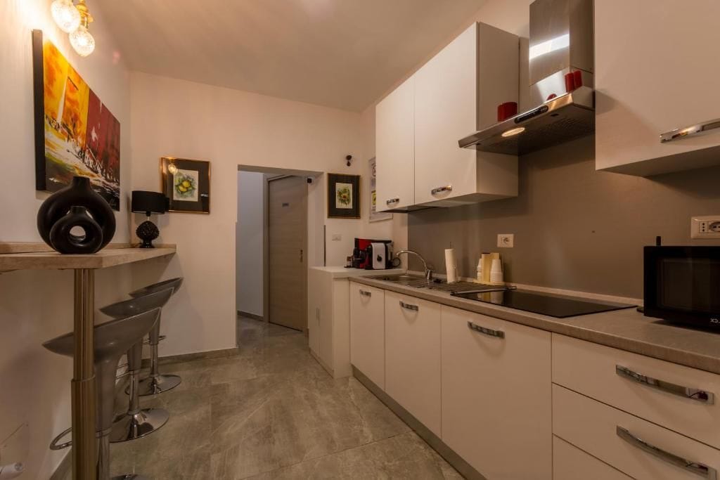 Una cucina moderna con mobili bianchi, un forno a microonde nero e una cappa aspirante in acciaio inossidabile.