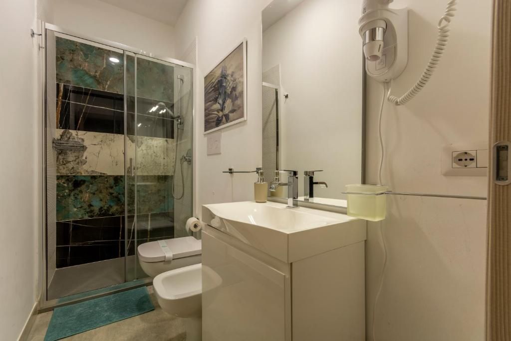 Un bagno con cabina doccia in vetro, un water, un lavandino con specchio e un telefono.