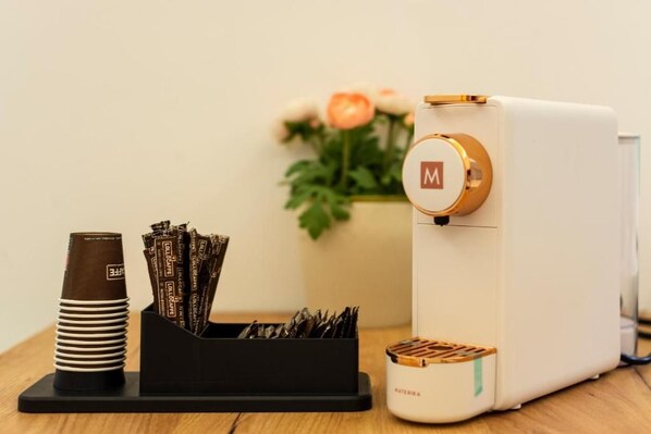 A coffee machine with a white and gold design, a coffee cup, and a container with coffee pods on a wooden surface.