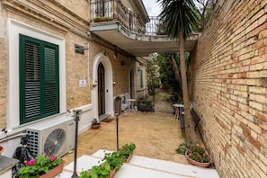 Une cour avec un mur en briques, une porte blanche et un balcon doté d’une balustrade en métal.