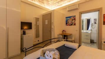 A hotel room with a bed, a desk, a chair, a television, and a bathroom visible through an open door.