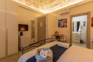 Habitación de hotel con cama, escritorio, silla, televisor y baño visible a través de una puerta abierta.