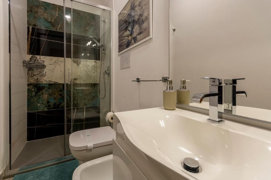 Une salle de bain avec une douche à parois de verre, des toilettes blanches, un grand lavabo blanc avec un miroir et un distributeur de serviettes de couleur beige.