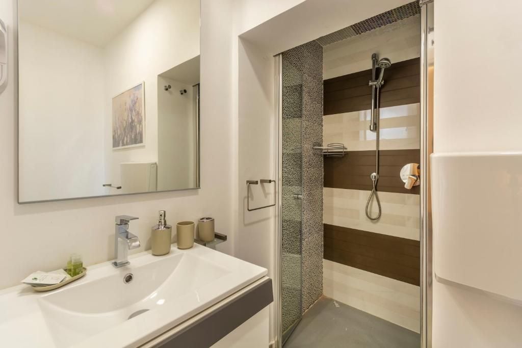 Un baño moderno con un espejo grande, un lavabo blanco y una ducha con cerramiento de vidrio.