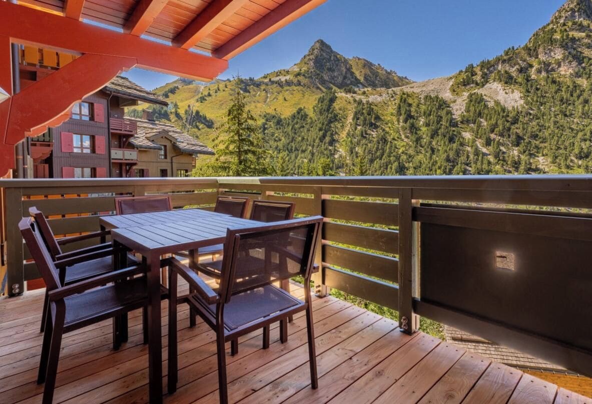 A wooden deck with a table and chairs, overlooking a mountainous landscape.