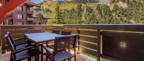 A wooden deck with a table and chairs, overlooking a mountainous landscape.