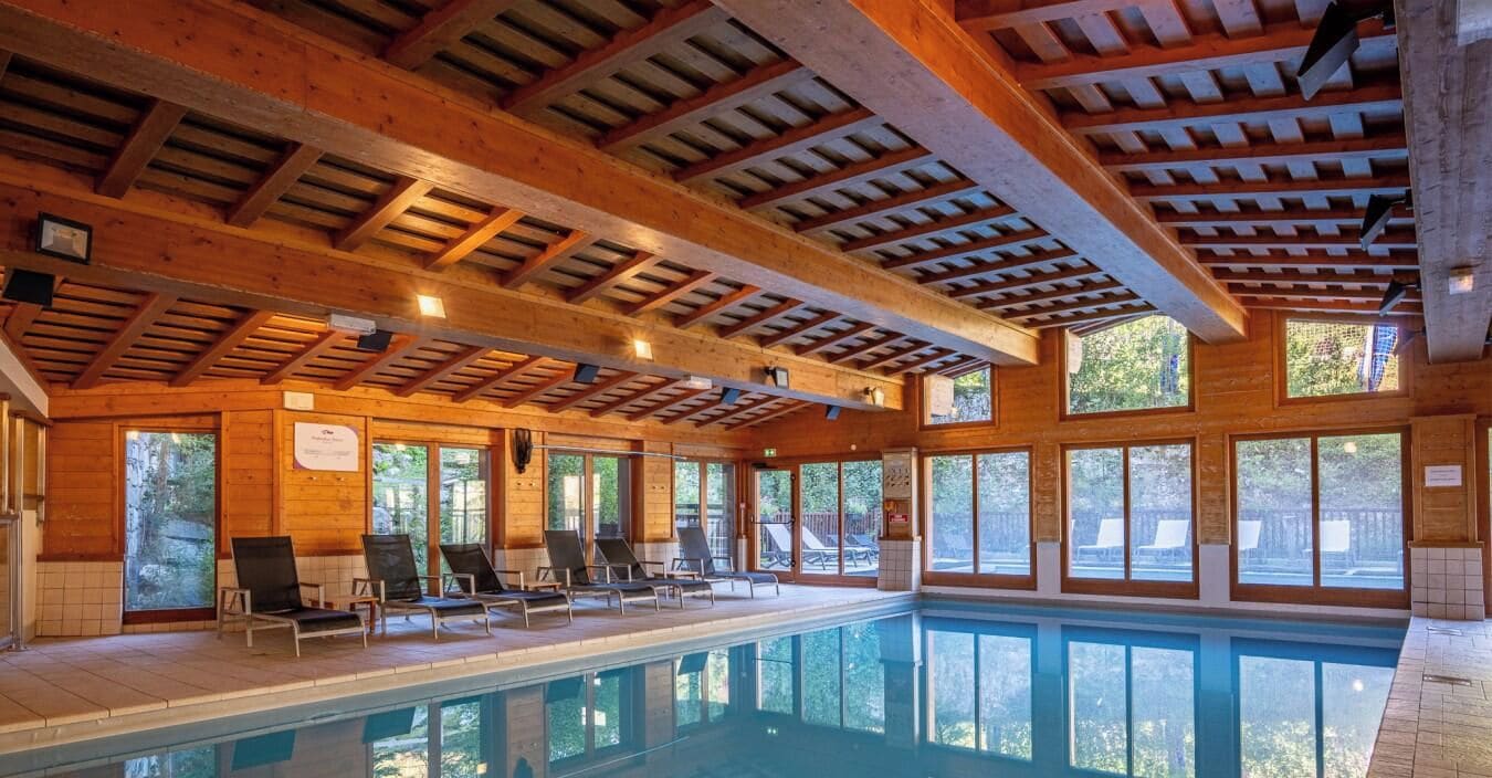 Une piscine intérieure avec des poutres en bois et de grandes fenêtres.
