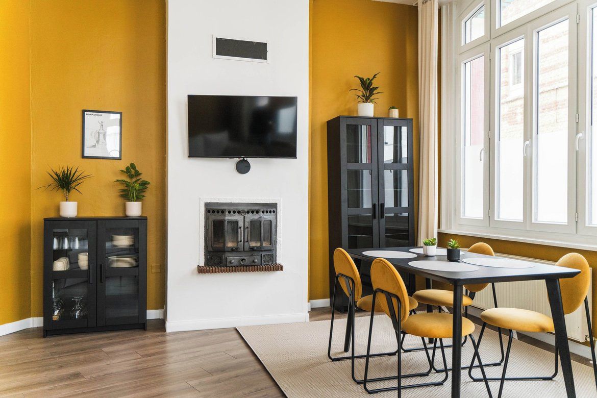 Ein modernes Wohnzimmer mit Kamin, einer Essecke mit gelben Stühlen, einem schwarzen Schrank und einem an der Wand befestigten Fernseher.