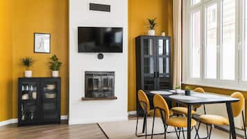 Ein modernes Wohnzimmer mit Kamin, einer Essecke mit gelben Stühlen, einem schwarzen Schrank und einem an der Wand befestigten Fernseher.