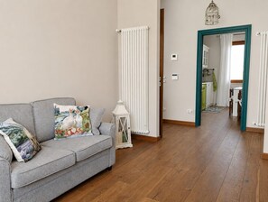 En stue med en grå sofa, en hvid radiator og trægulv.