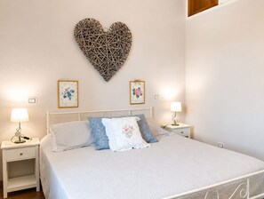 A bedroom with a bed, two bedside tables, a wall-mounted heart-shaped decoration, and two framed floral pictures. - A villa for exclusive use, in the countryside, secluded yet close to major cities (Toscana)