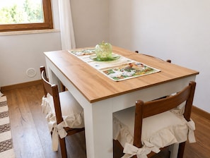 A dining table with a placemat, chairs with white cushions, and a window with curtains. - A villa for exclusive use, in the countryside, secluded yet close to major cities (Toscana)