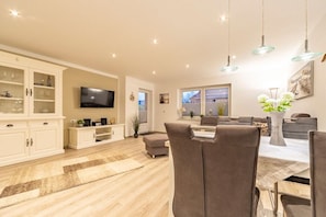 A spacious living room with a flat-screen TV, a dining area with a table and chairs, and a kitchen area with cabinets and a countertop. - Holiday apartment with 2 bedrooms (Norddeich)