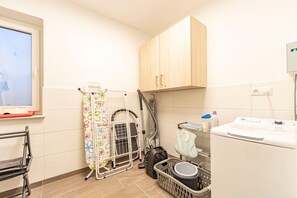 A laundry area with a washing machine, a drying rack, a vacuum cleaner, and a window with a view. - Holiday apartment with 2 bedrooms (Norddeich)