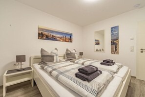 A hotel room with two beds, a nightstand, a lamp, and a painting on the wall. - Holiday apartment with 2 bedrooms (Norddeich)