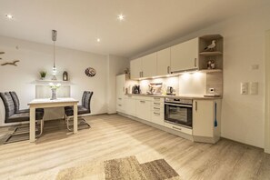 A modern kitchen with white cabinets, a built-in oven, and a dining area with a table and chairs. - Holiday apartment with 2 bedrooms (Norddeich)