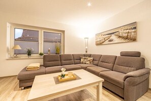 Uma sala de estar moderna com sofá seccional, mesa de centro, luminária e um quadro na parede.