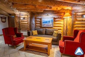 A log cabin interior with a sofa, two armchairs, a wooden coffee table, and a lamp. - 2 Bed Apartment - ski in ski out - Arc 1950 - Auberge Jerome (Arc 1950)