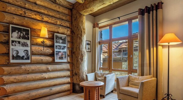 Ein rustikales Holzhaus-Interieur mit Kamin, einem runden Holztisch, zwei Sofas und einem großen Fenster mit Vorhängen.
