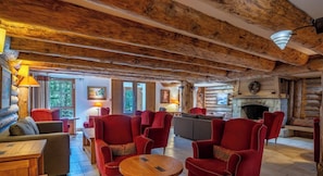 Ein Blockhaushaus-Interieur mit Kamin, roten Polstersesseln und einem Holzesstisch.