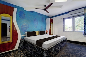 A hotel room with a bed, a ceiling fan, a window with curtains, and a wall with a unique blue and red design. - Collection Sirkazhi Formerly Navagiragat (Chennai)
