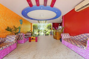 A brightly colored lobby with two sofas, a small table, and a reception desk. - Collection Sirkazhi Formerly Navagiragat (Chennai)