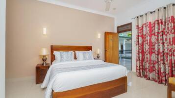 Quarto com cama de madeira, duas luminárias de cabeceira, ventilador de teto e vista para o exterior por uma porta.