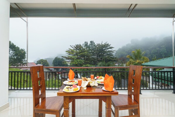 Una mesa de madera preparada para el desayuno en un balcón con vista a un paisaje brumoso.