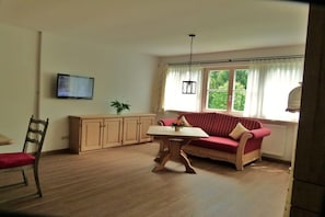 A living room with a sofa, a table, a chair, a television, and a window with curtains. - Holiday apartment with 2 bedrooms (Bad Wiessee)