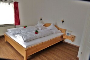 A single-bed room with a wooden frame, white bedding, and a small bedside table with a clock. - Holiday apartment with 2 bedrooms (Bad Wiessee)