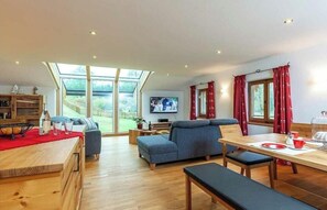 A spacious living area with a wooden dining table, a sofa, and a television. - Holiday apartment with 1 bedroom (Unterwössen)