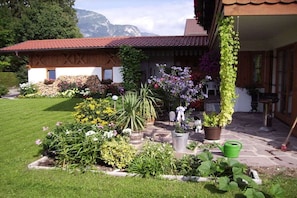 A house with a red-tiled roof, surrounded by a well-maintained garden with various plants and flowers. - Holiday apartment with 1 bedroom (Garmisch-Partenkirchen)
